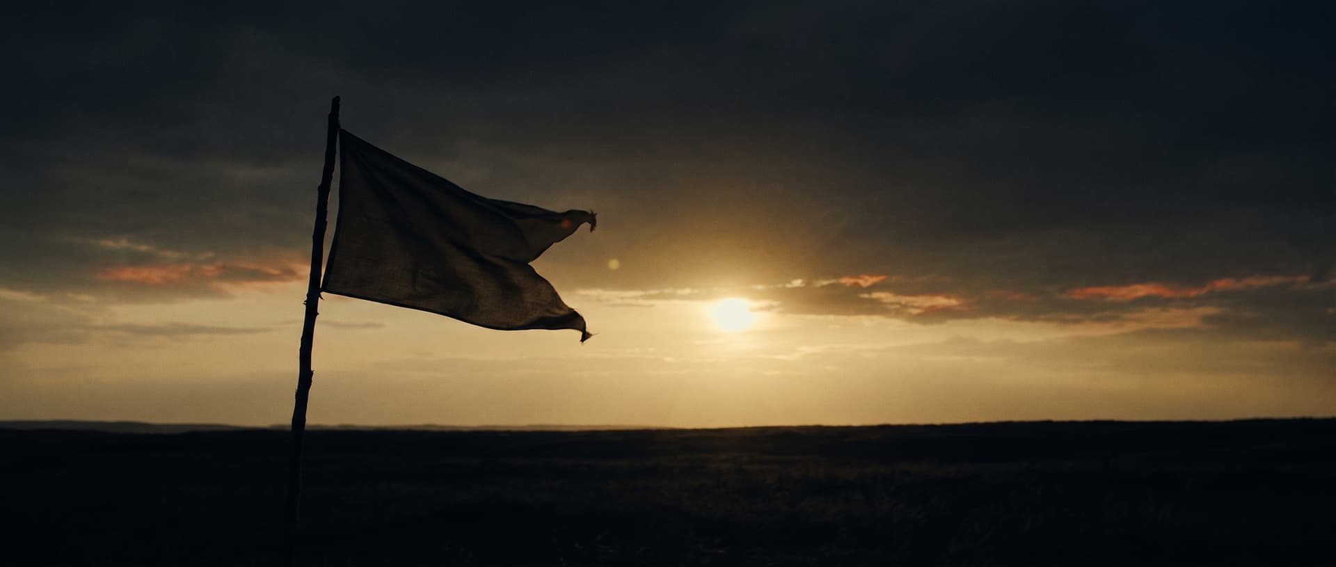 A pennant flag against a dark horizon under a low brass sun