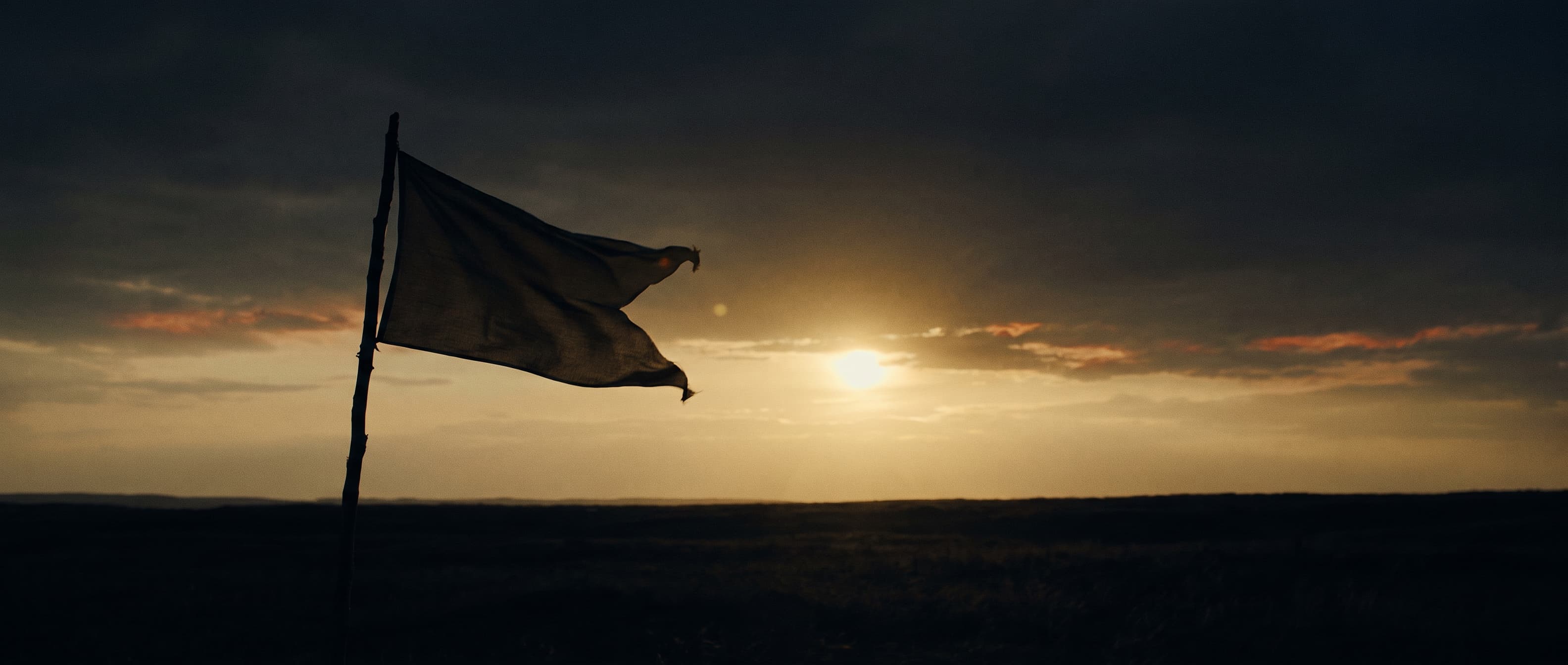 A pennant flag against a dark horizon under a low brass sun